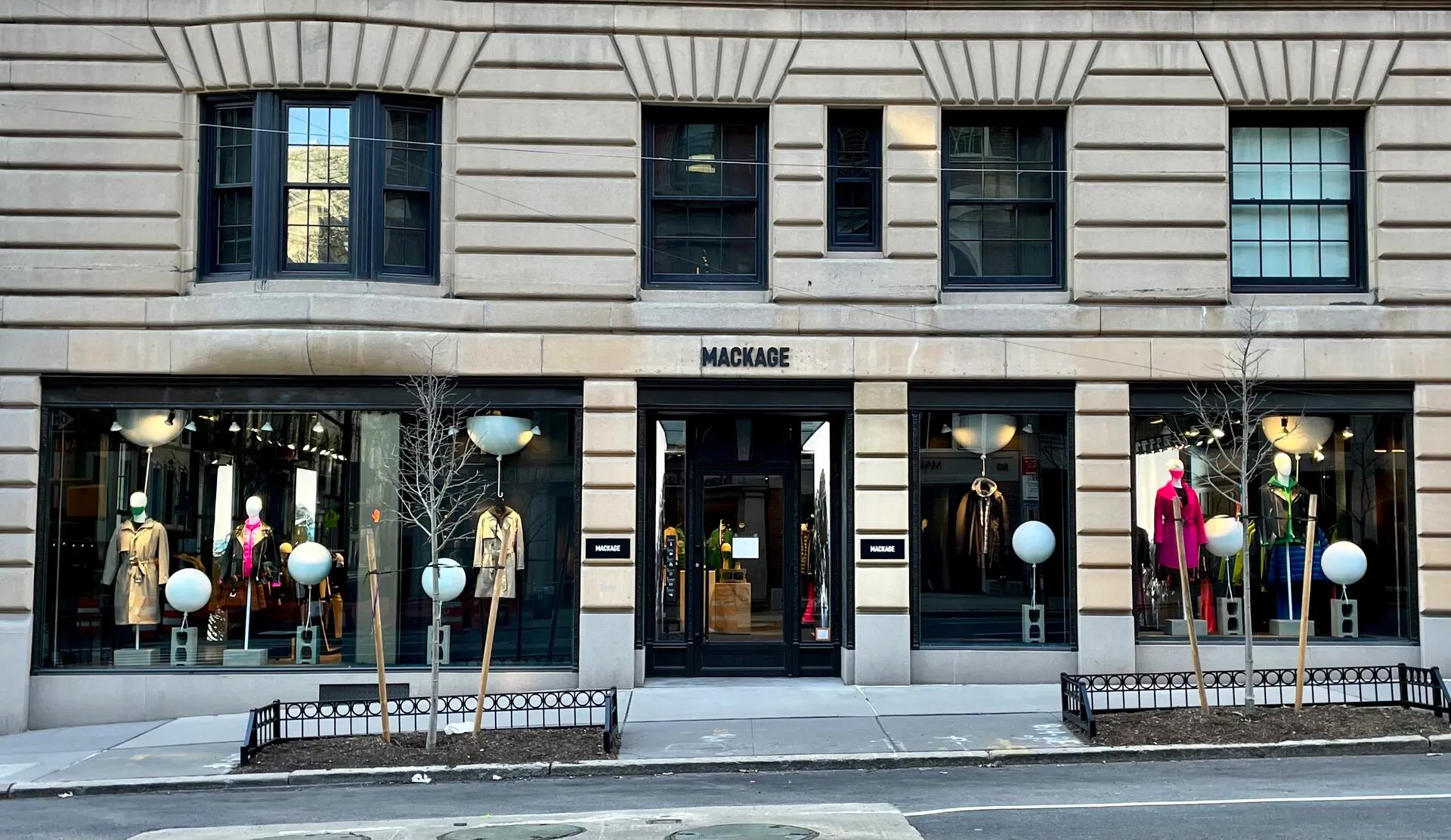 Mackage storefront on a limestone facade, its windows styled with spring outerwear and oversized white globes.